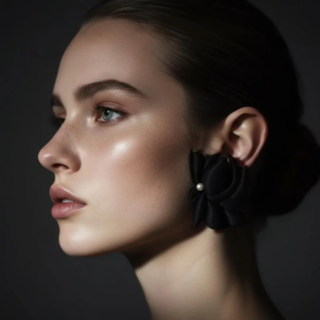 Woman wearing large black flower-shaped earring with pearl accent, side profile