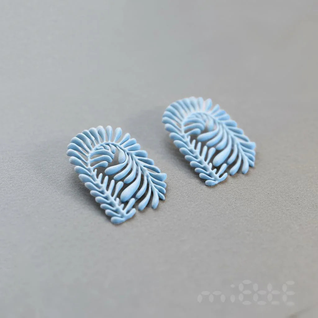 Artisan light blue leaf-shaped earrings with intricate details on a gray background