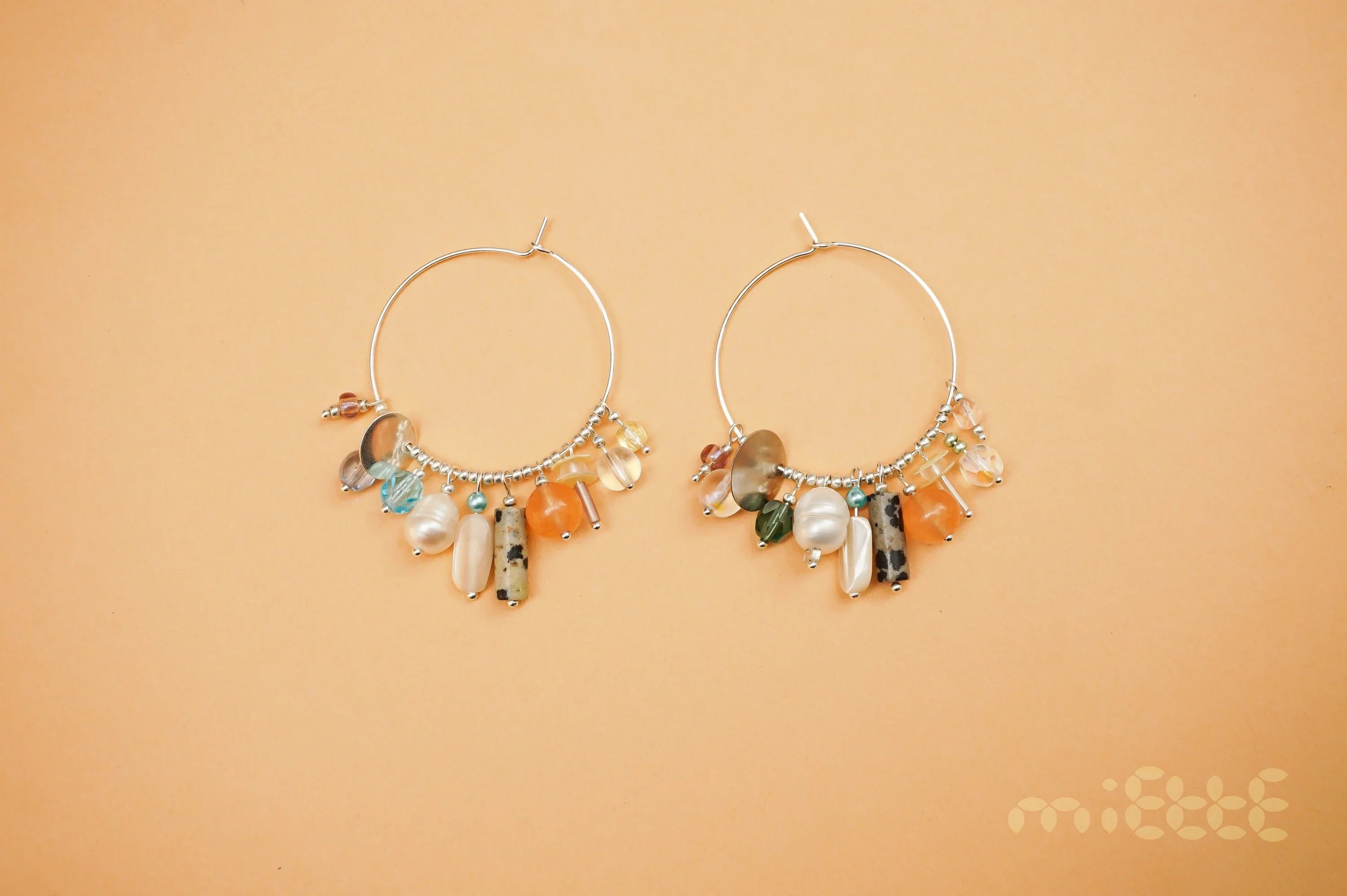 Handcrafted hoop earrings with colorful gemstone and pearl charms on peach background