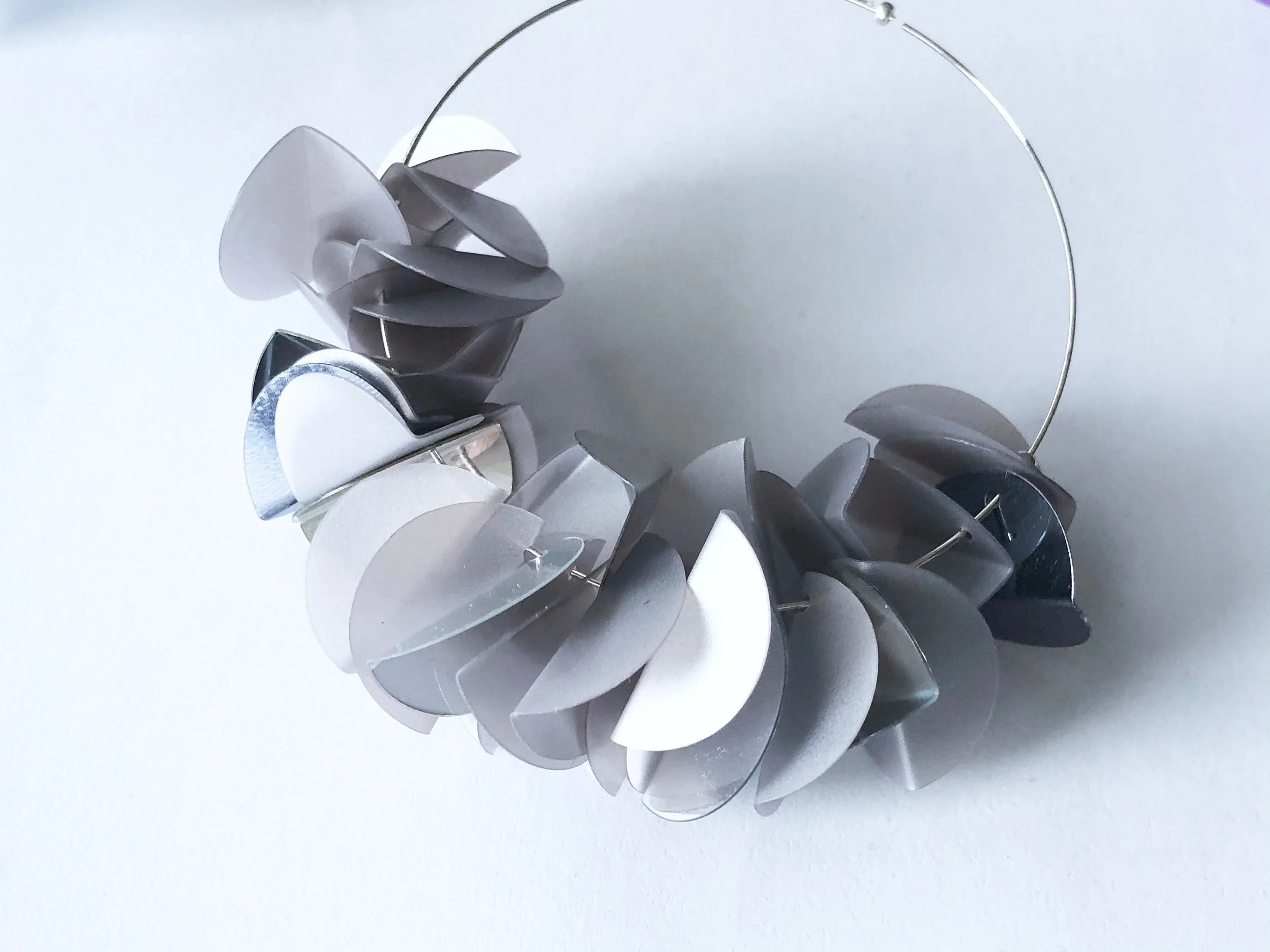 Contemporary hoop earring with layered silver and gray geometric discs on white background