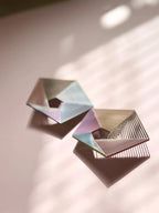 Geometric pastel earrings with open hexagonal design on a soft pink background