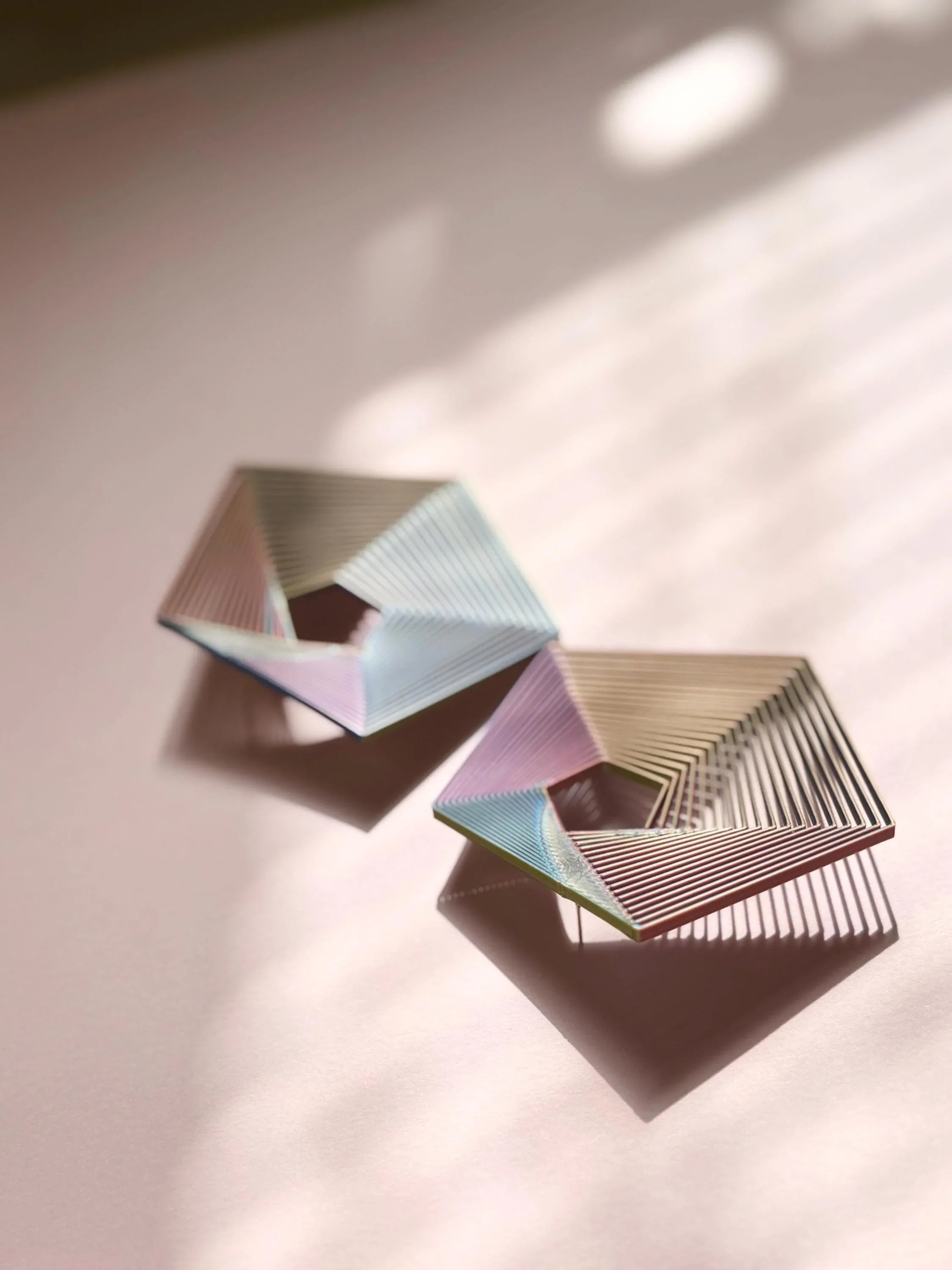 Geometric pastel earrings with open hexagonal design on a soft pink background