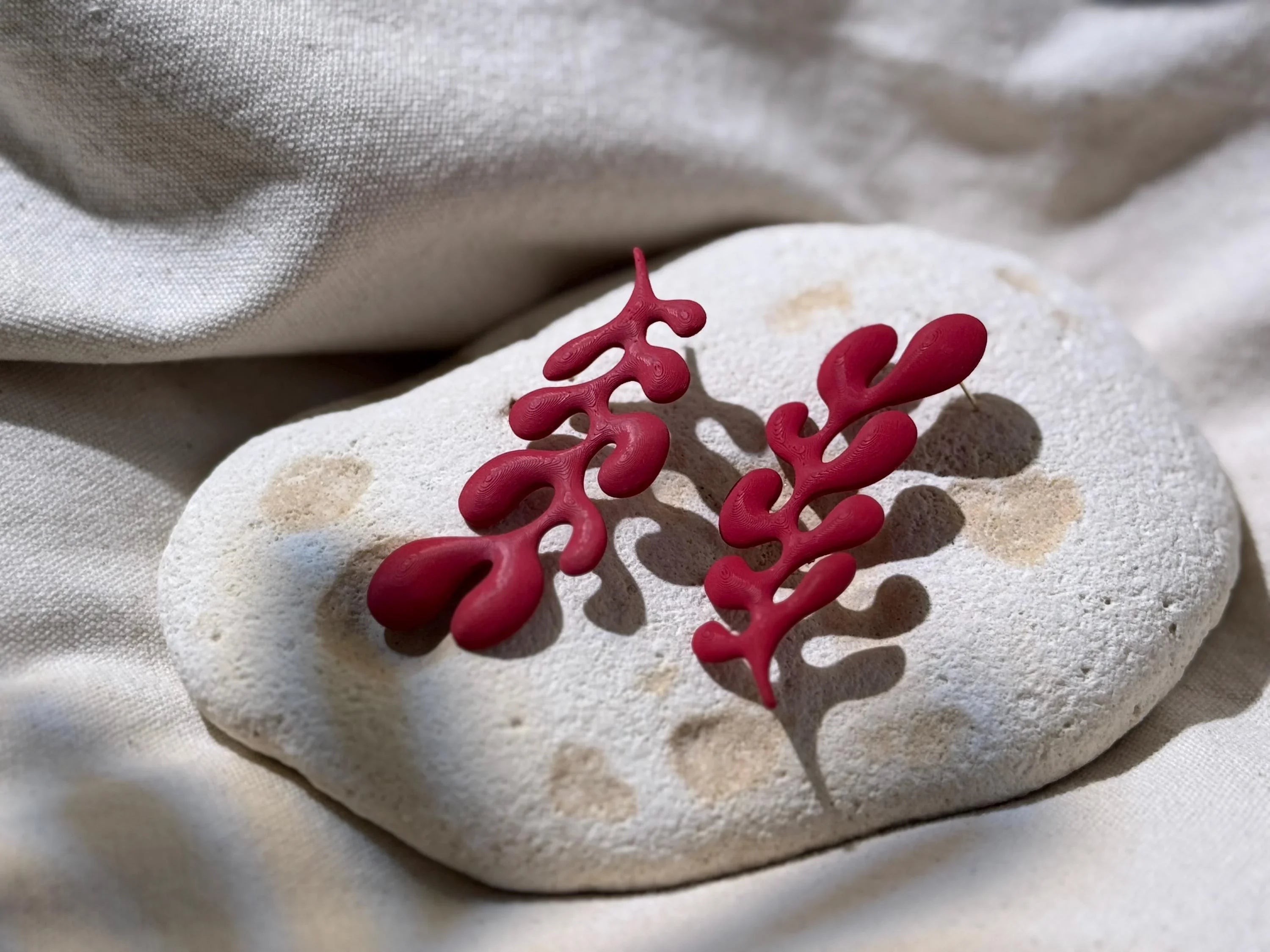 Unique red sculptural earrings with organic shapes, displayed on a textured stone