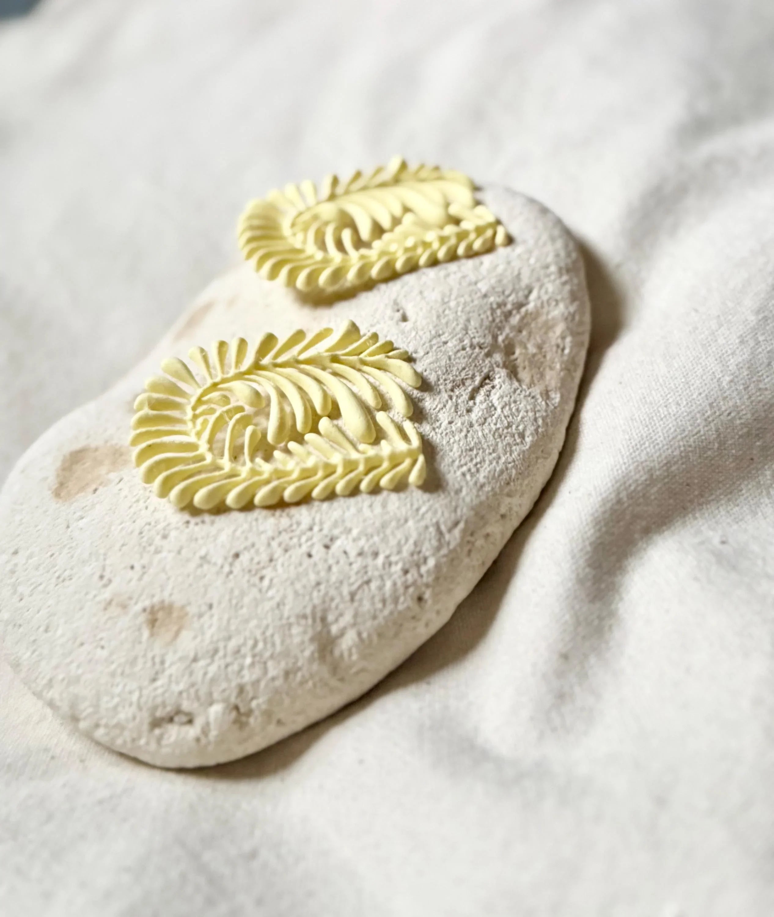 Pair of yellow leaf-shaped earrings with textured details on a white stone, artisanal jewelry