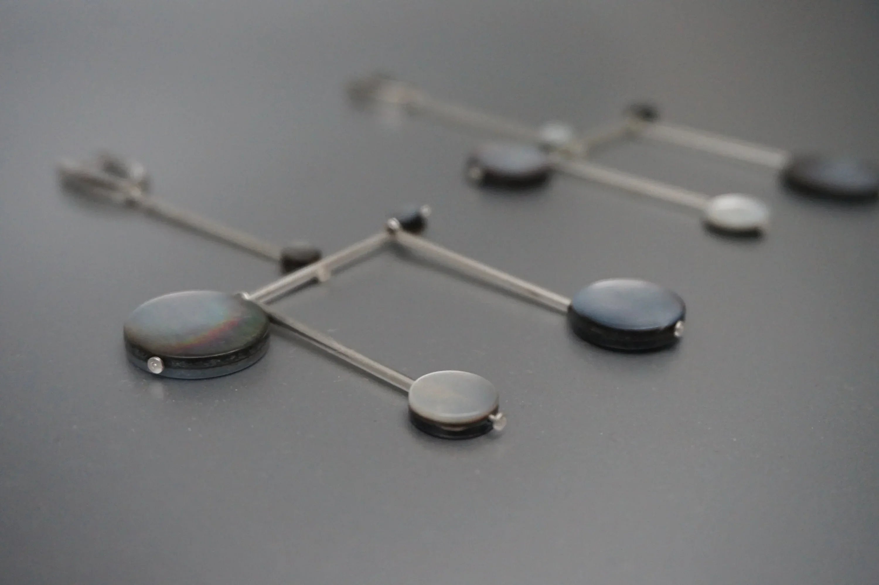 Modern geometric dangle earrings with black and gray circular accents on metal rods