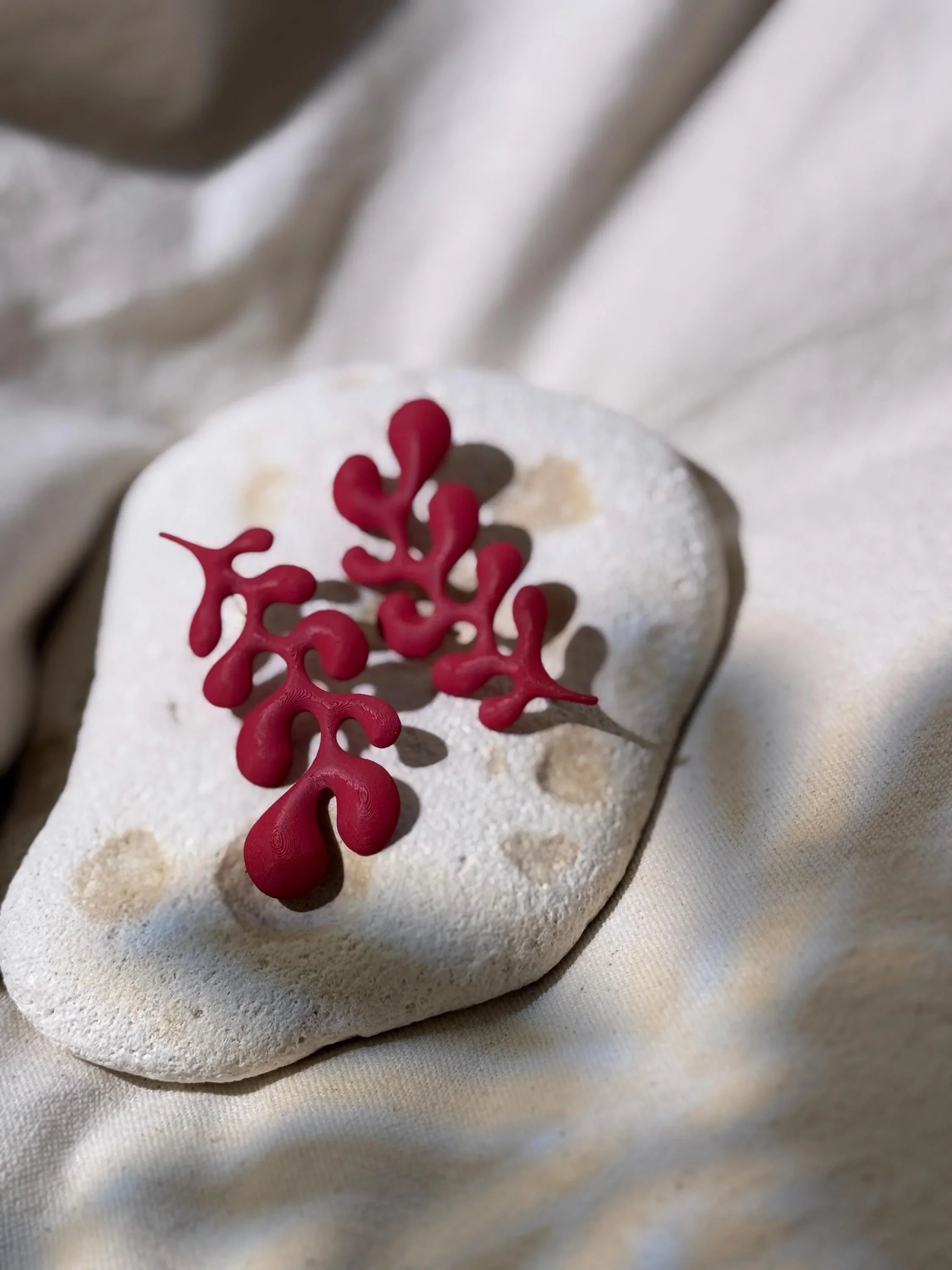 Red abstract artisanal brooch with organic shapes on textured stone and fabric background