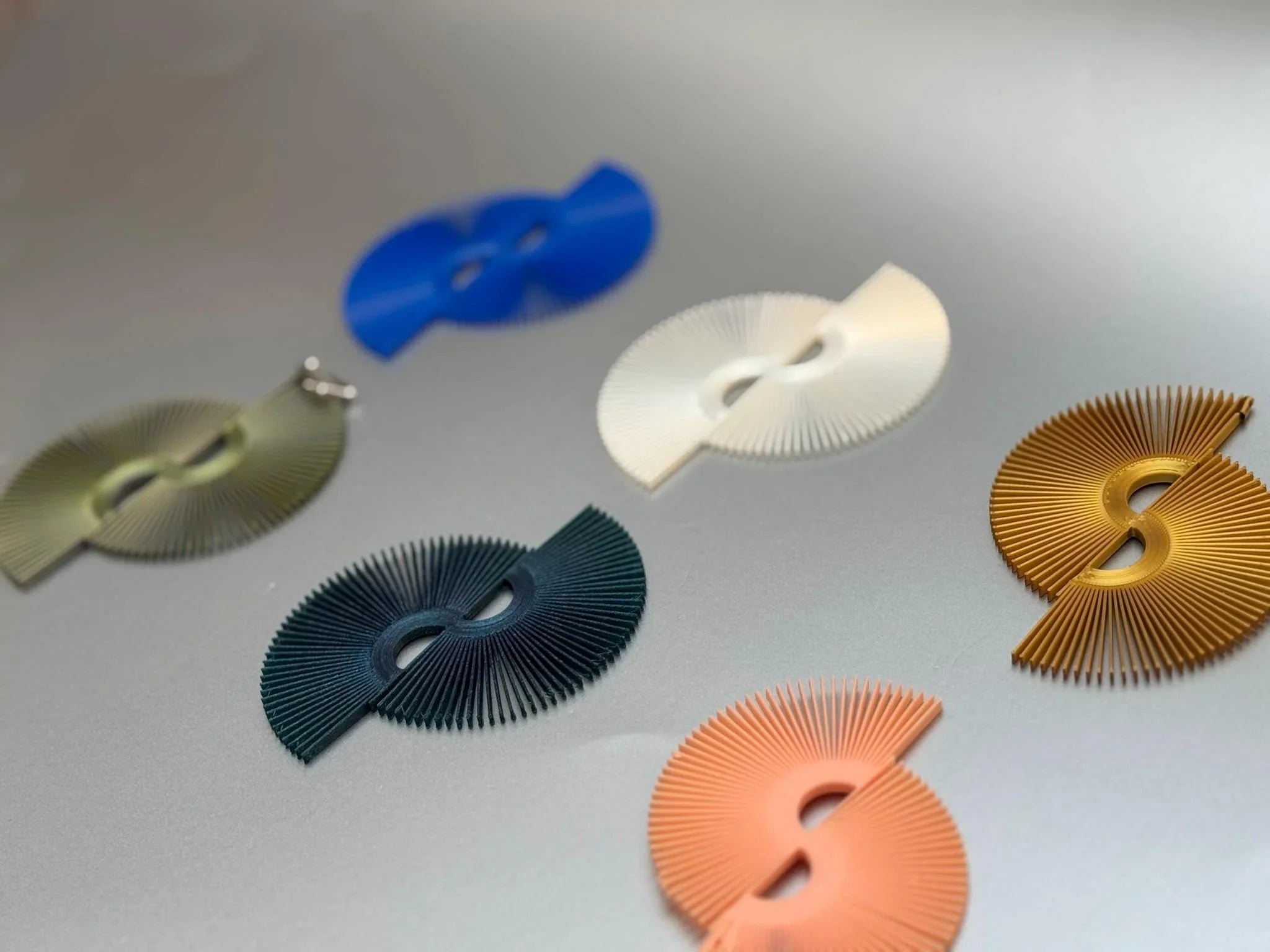 Colorful modern fan-shaped earrings in blue, ivory, green, gold, and peach on a gray background