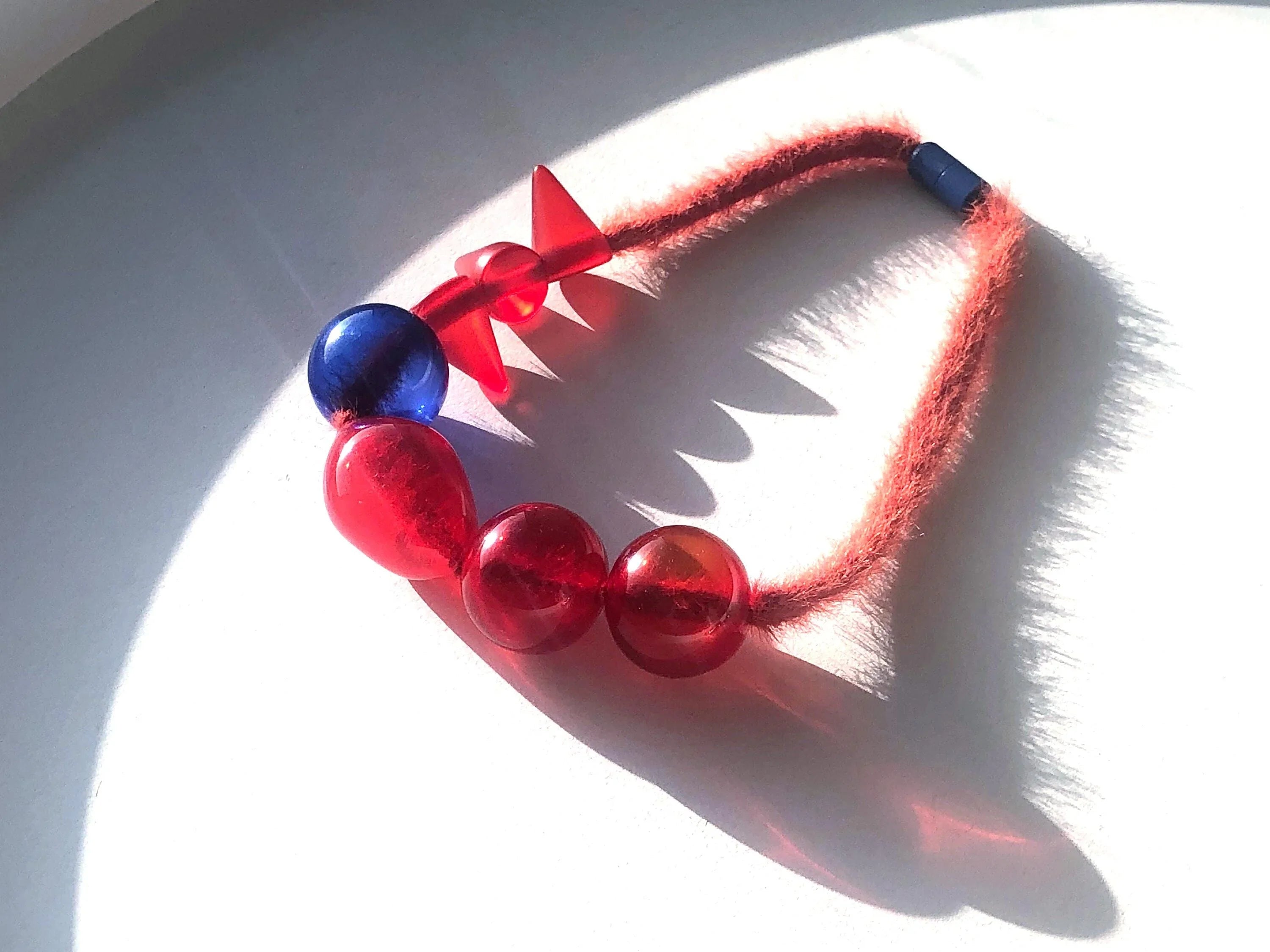Handcrafted necklace with red and blue resin beads on a fuzzy red cord, artisan jewelry