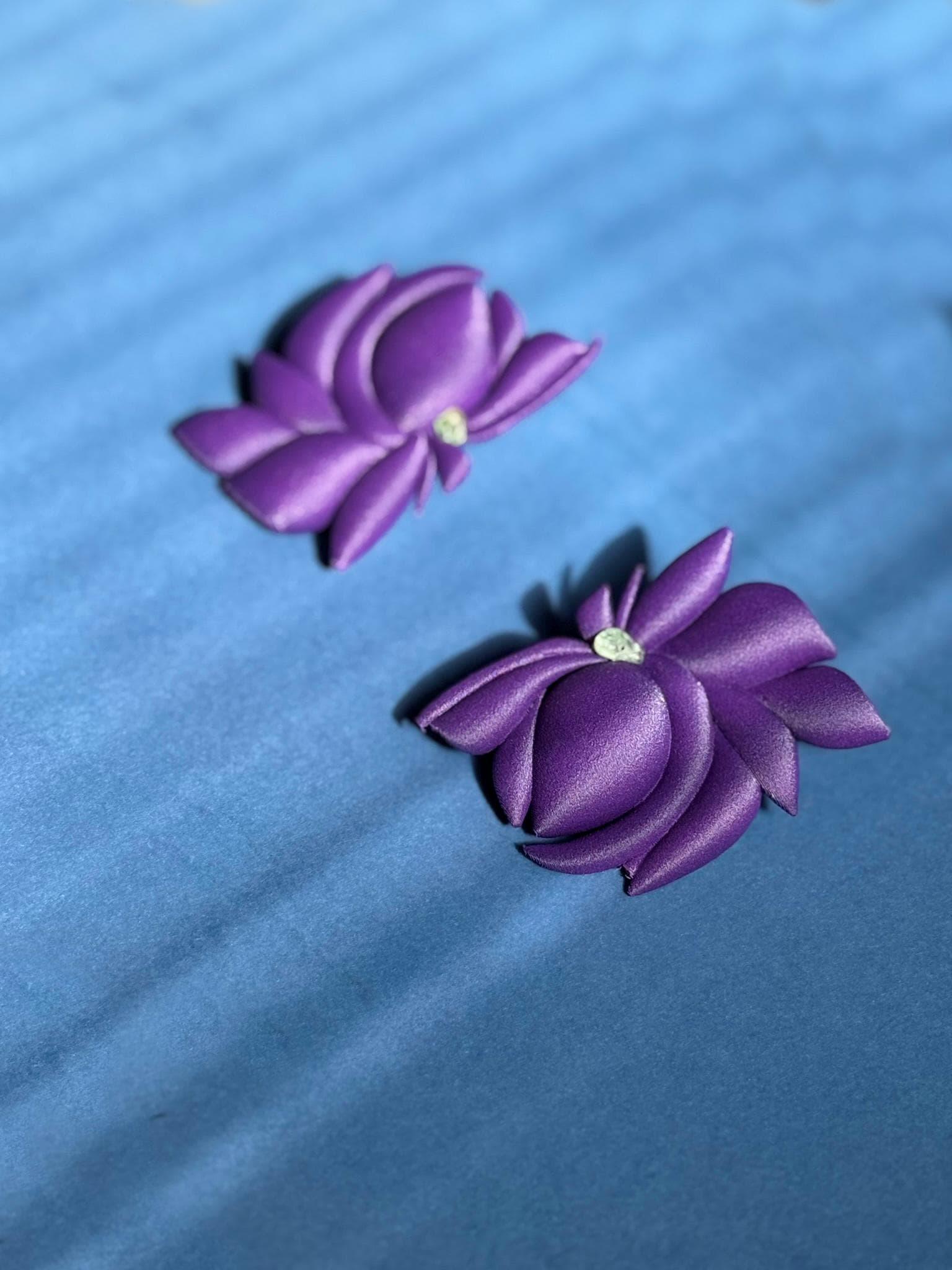 Pair of handmade purple flower earrings with petal details on a blue background