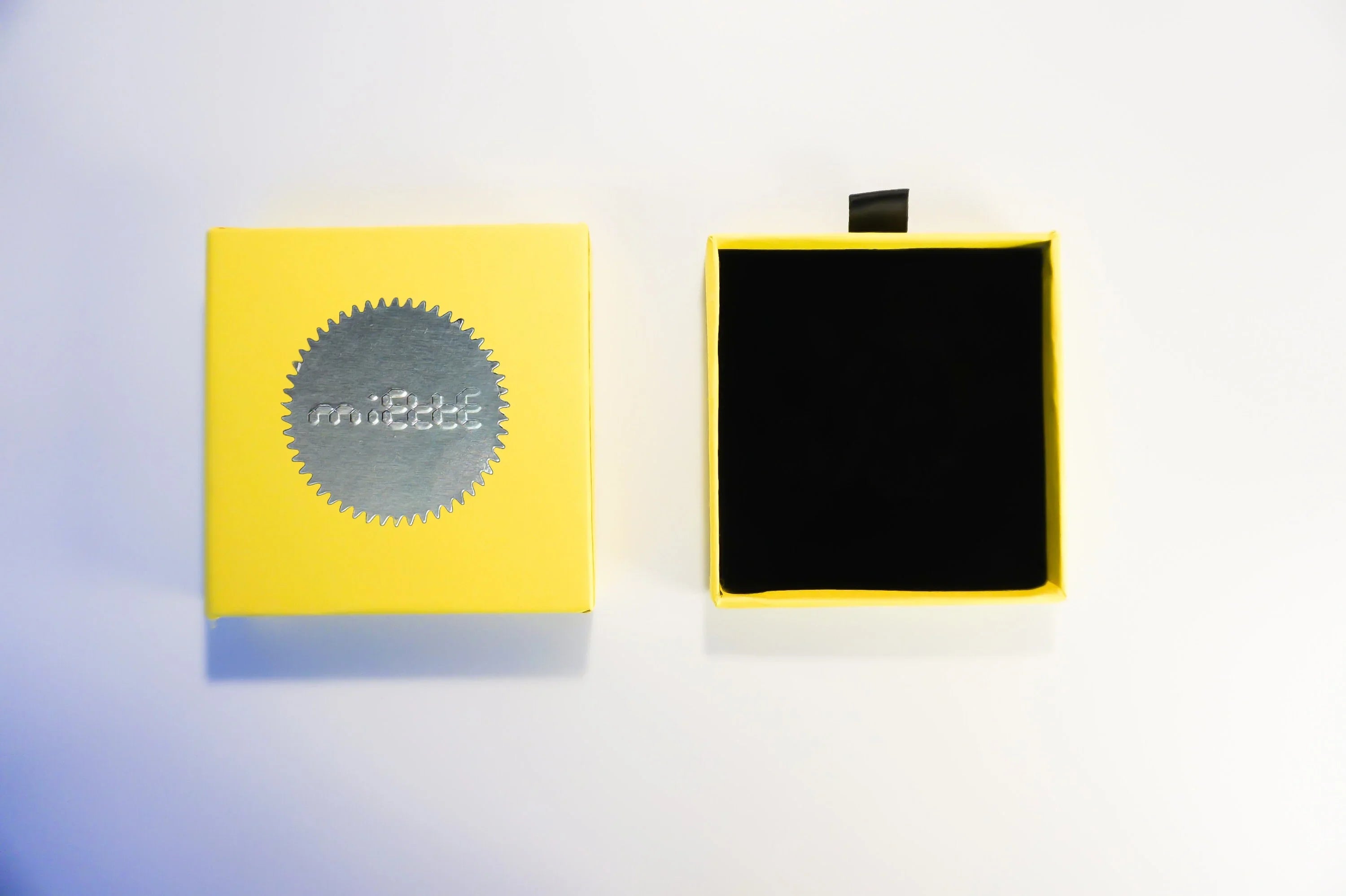 Yellow jewelry box with silver embossed design, open to show black interior on white background