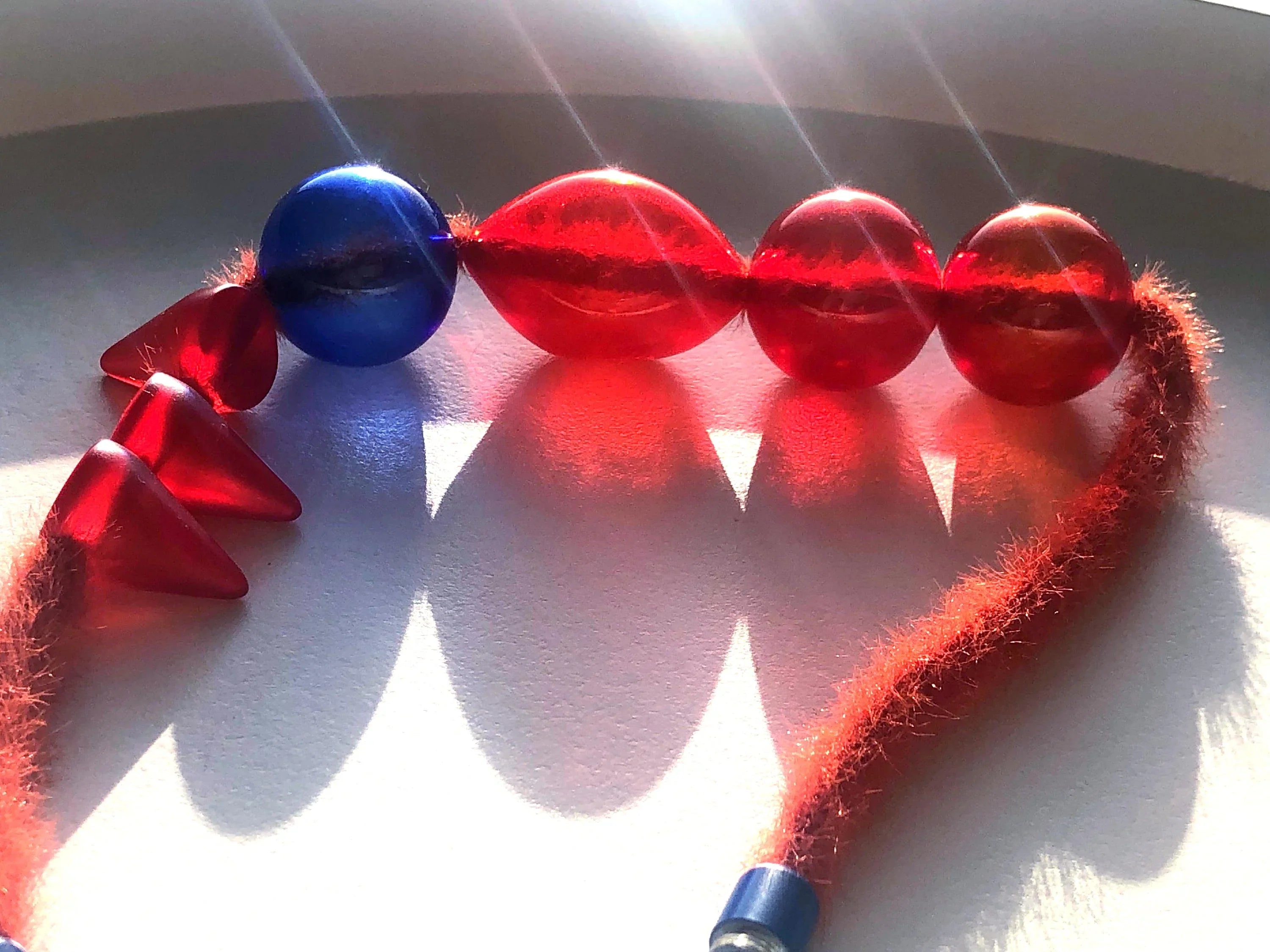 Handcrafted necklace with red and blue resin beads and textured red cord in sunlight