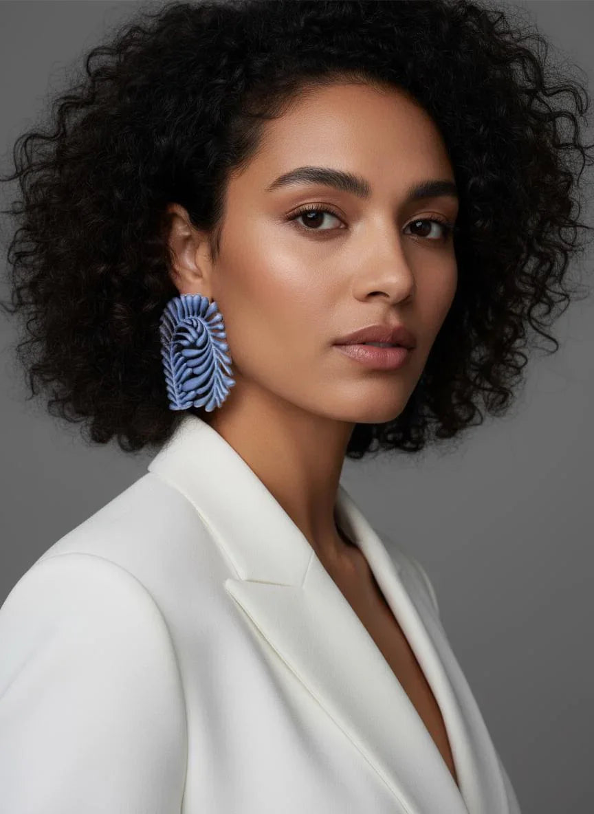 Woman in white blazer wearing large sculptural blue artistic earring, neutral background