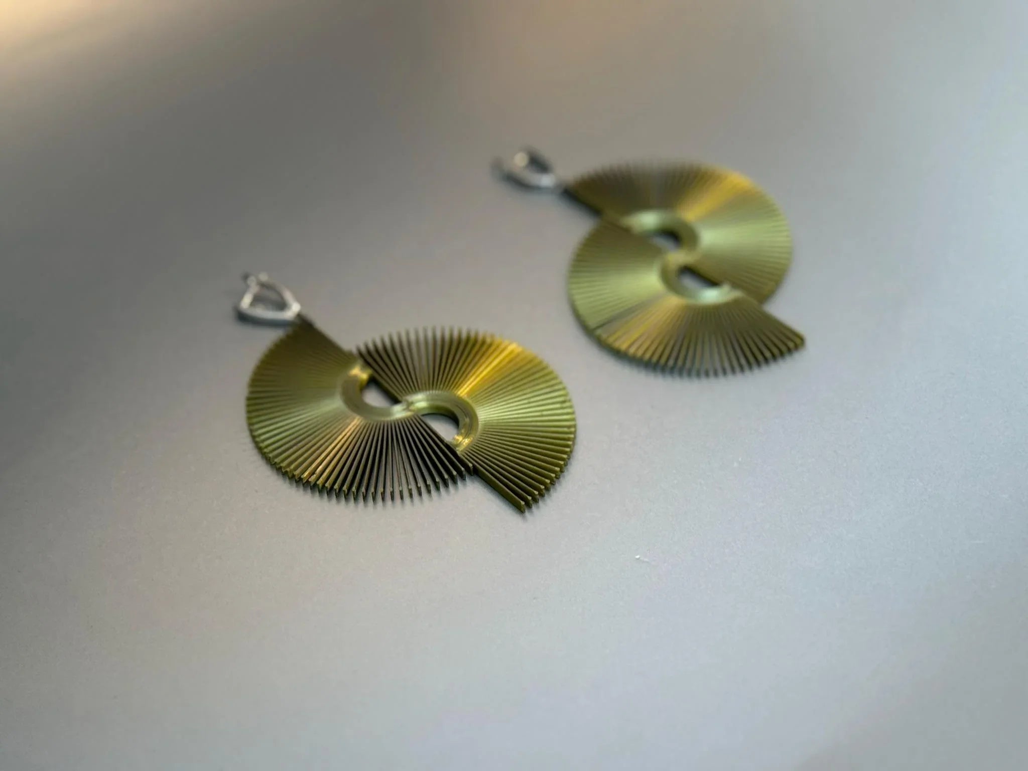 Gold fan-shaped statement earrings with geometric cutout design on a gray background