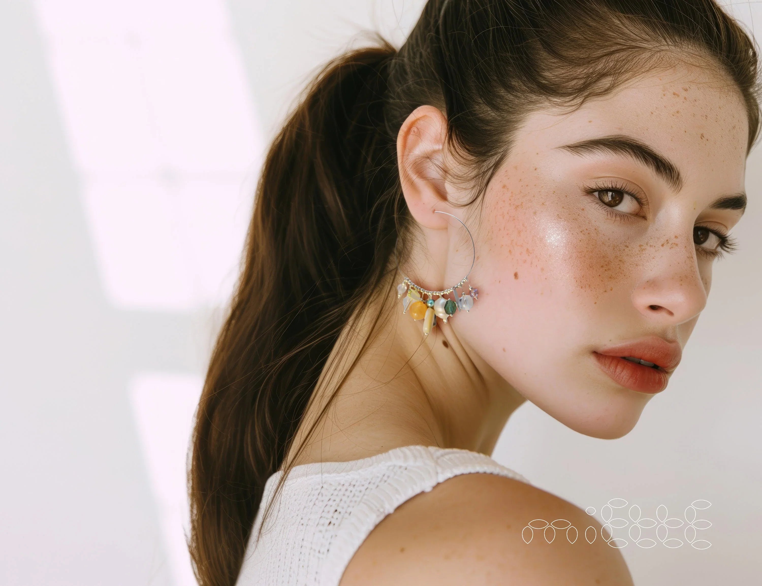 Woman wearing handmade colorful gemstone dangle earrings, minimal natural light setting