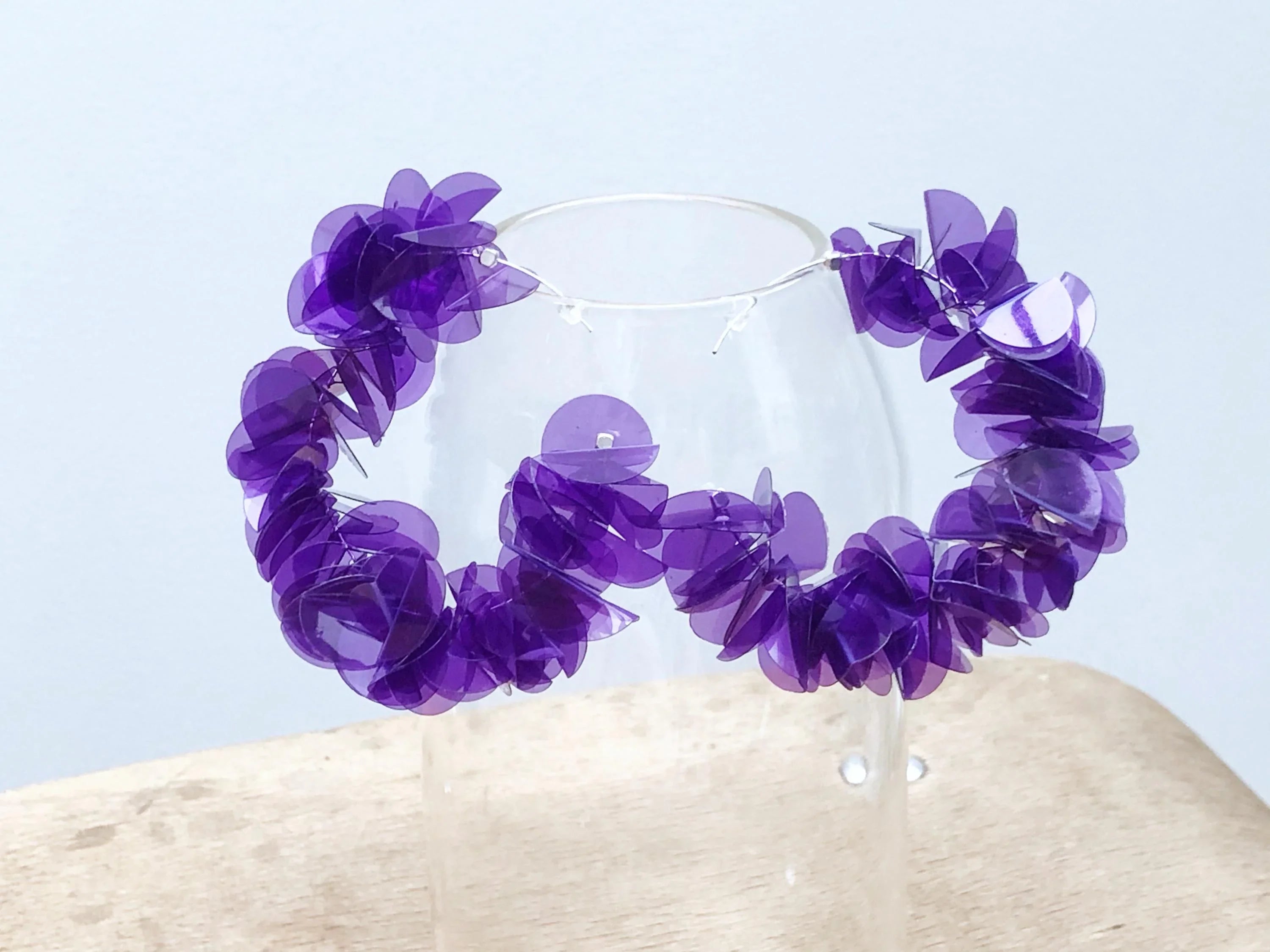 Purple translucent statement hoop earrings displayed on glass, artistic jewelry