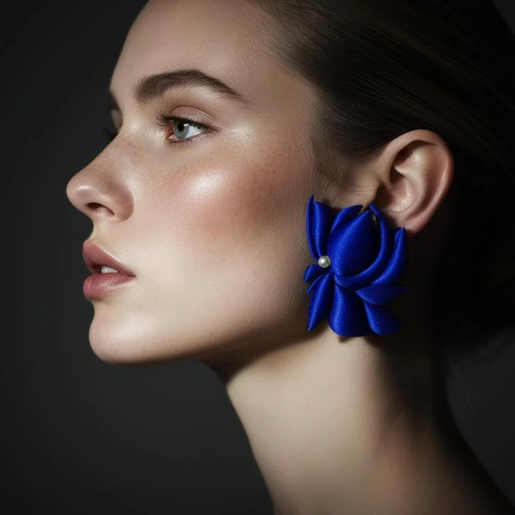 Woman wearing bold blue flower-shaped statement earring with pearl accent, side profile