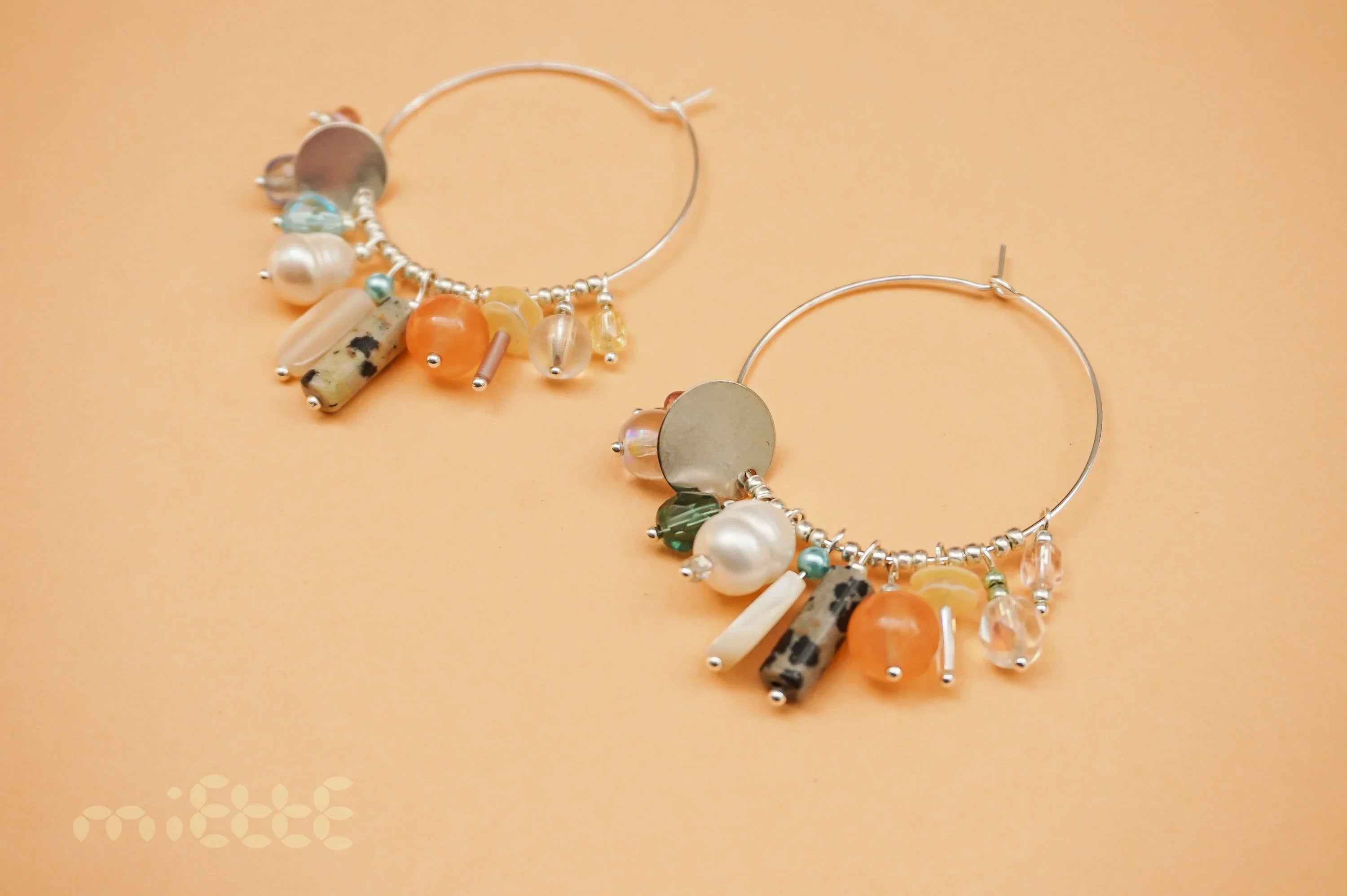 Silver hoop earrings with colorful gemstone, pearl, and bead charms on a peach background