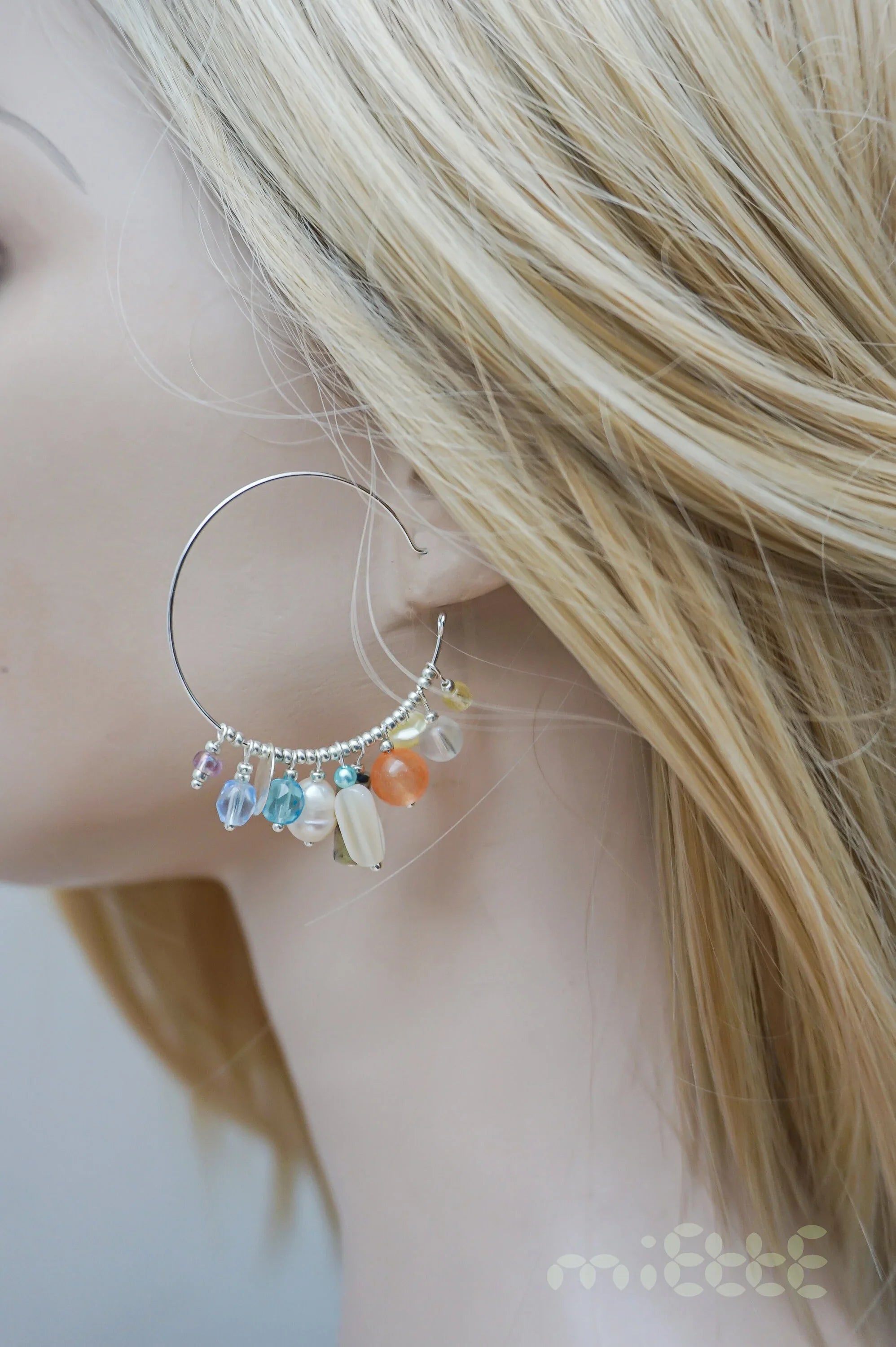 Large silver hoop earring with colorful beads and charms on mannequin ear
