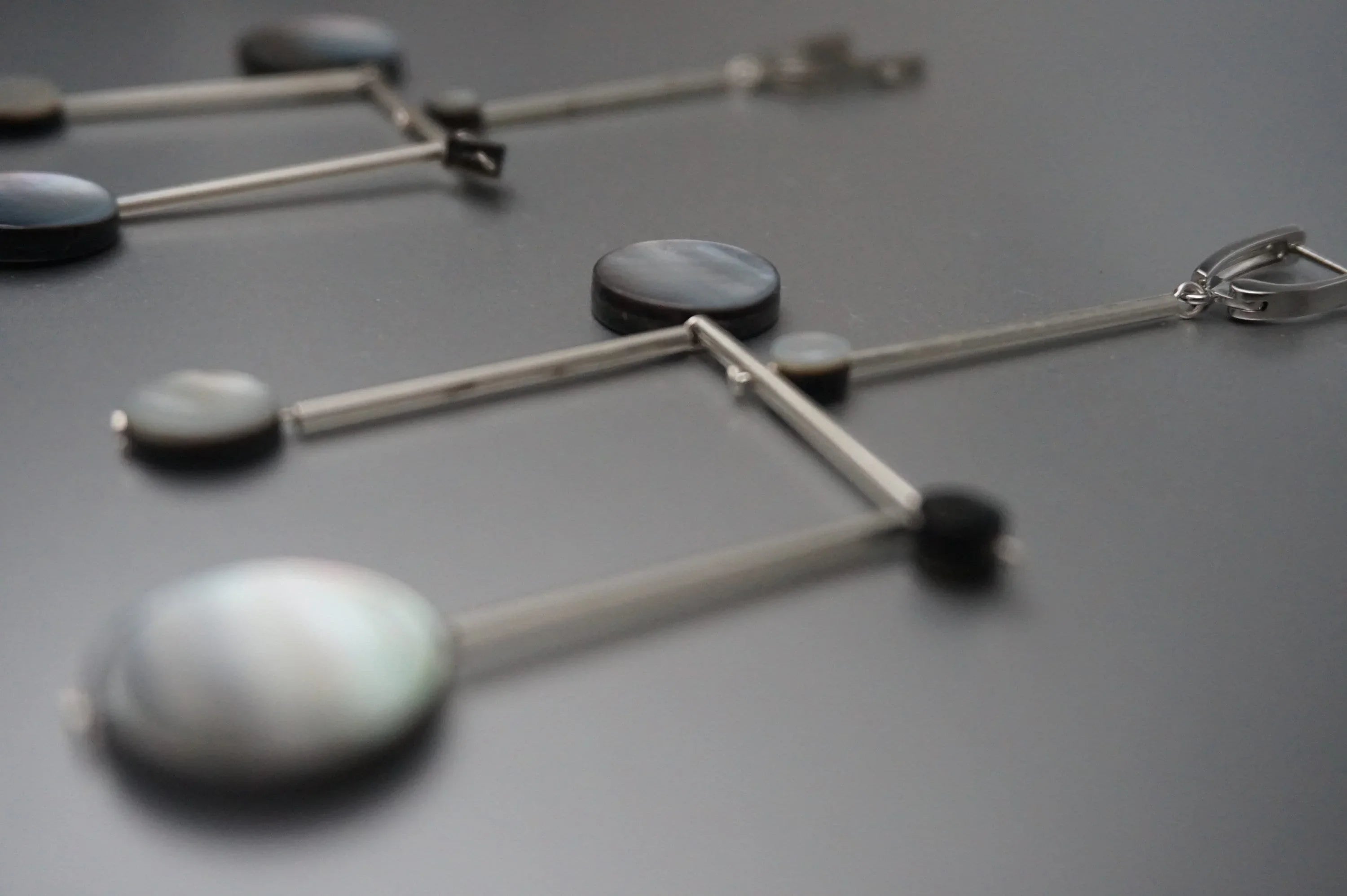Geometric dangle earrings with silver bars and round shell-like accents on dark surface