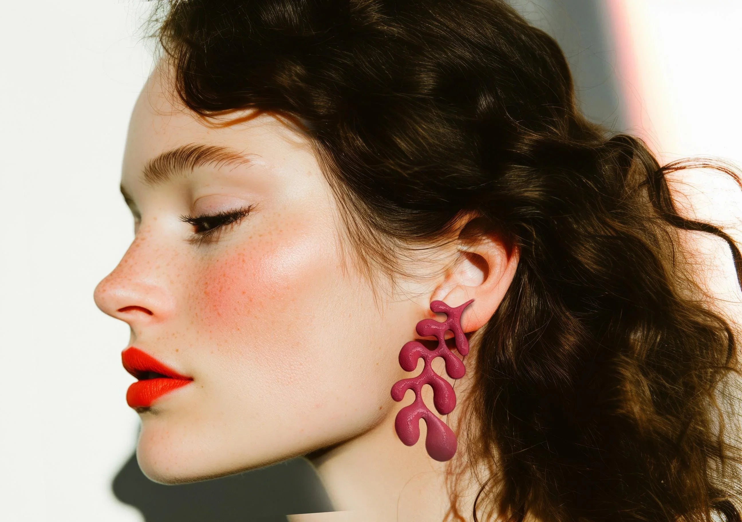 Woman wearing sculptural magenta statement earring, side profile, red lipstick