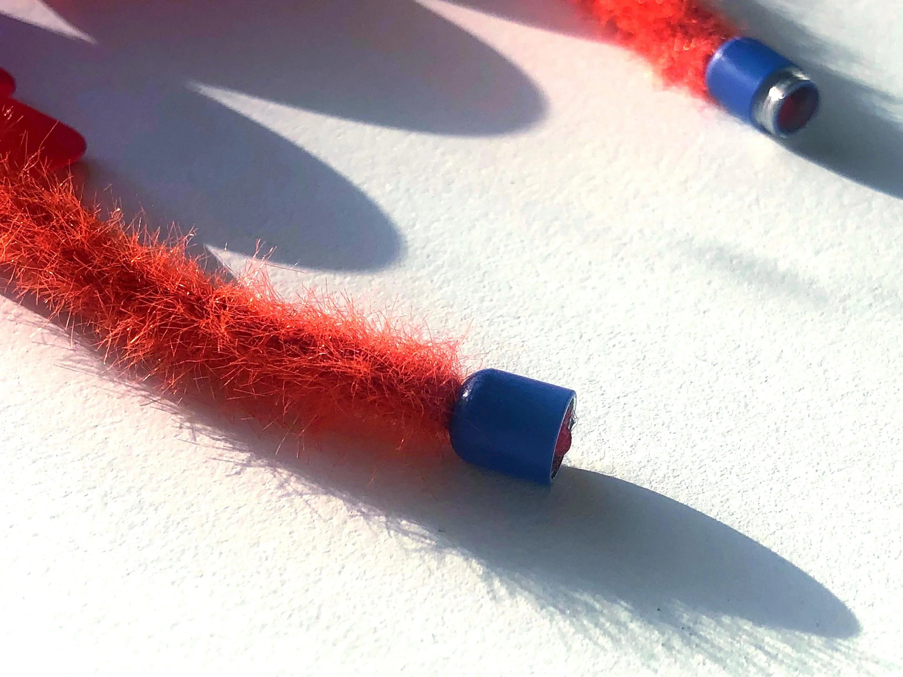 Close-up of a fuzzy orange necklace with blue metal ends on a white surface