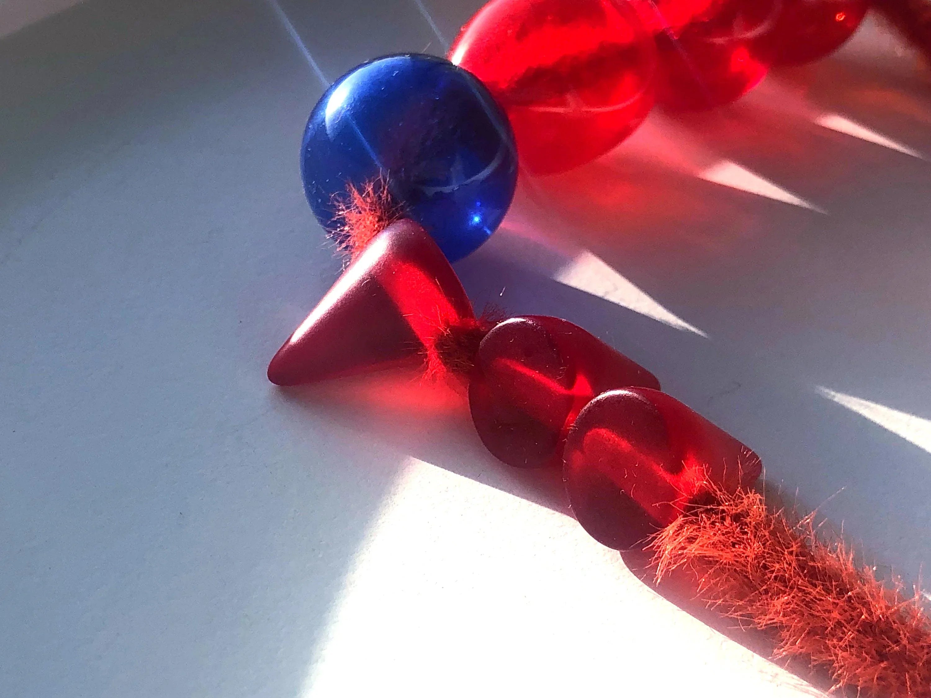 Close-up of red and blue artistic jewelry beads with soft fuzzy red thread in sunlight
