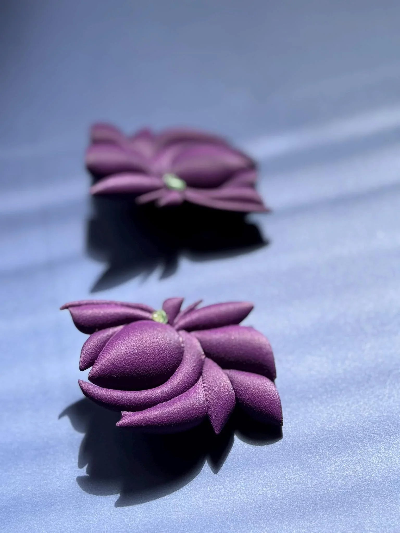 Violet flower-shaped earrings with textured petals and small green center on a blue surface