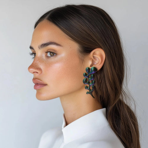 Woman wearing sculptural green statement earrings, profile view, minimalist background