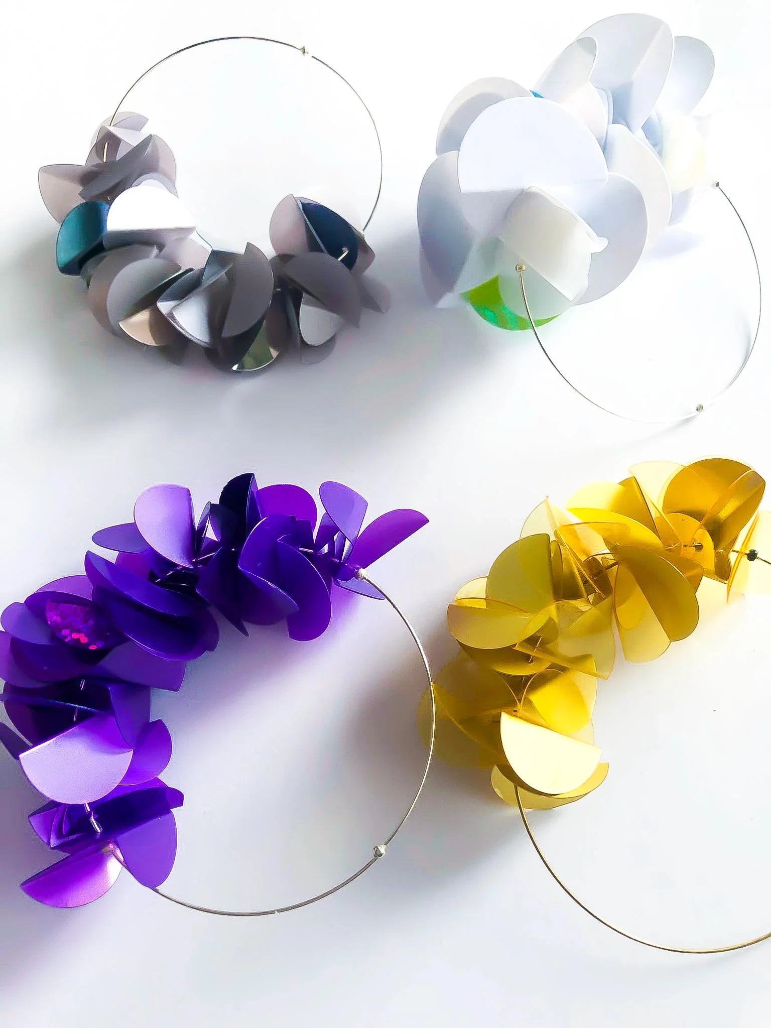 Colorful sculptural hoop earrings with layered petal-like shapes in silver, white, purple, and gold.