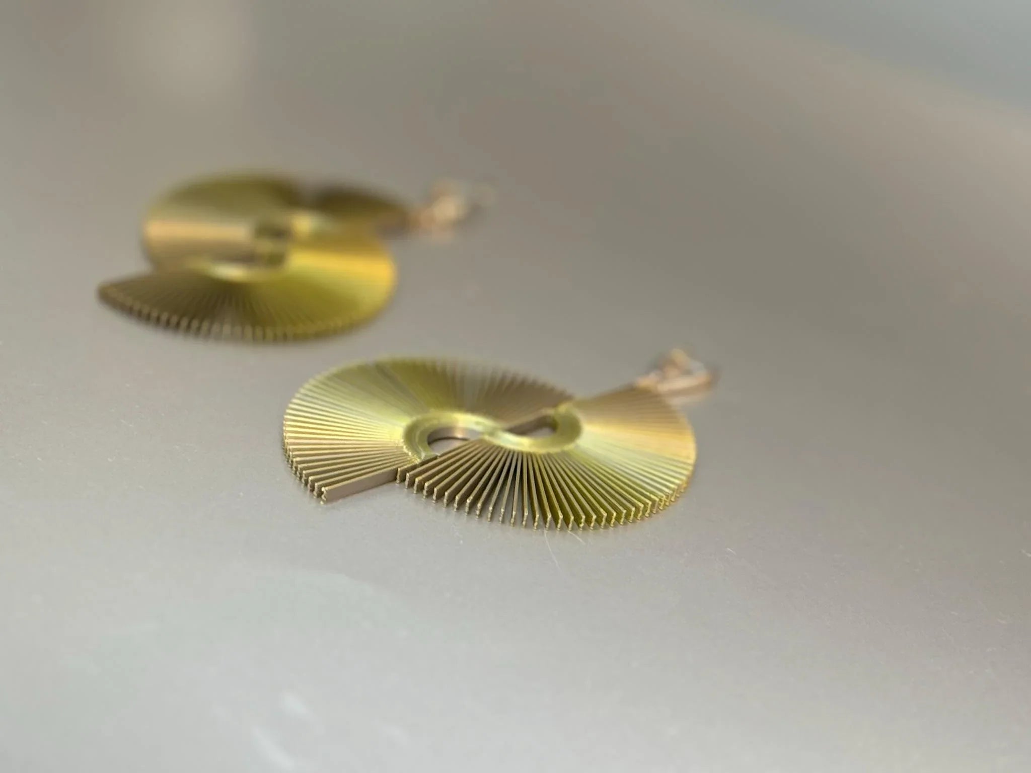 Artisan gold fan-shaped earrings with geometric cutout design on a neutral background