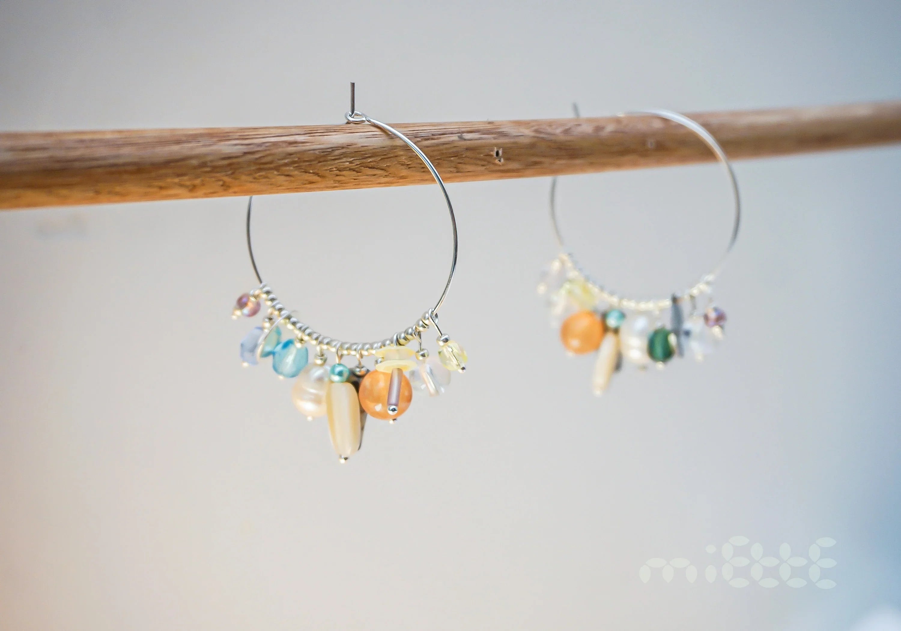 Handcrafted hoop earrings with colorful gemstone beads and pearls on a wooden rod