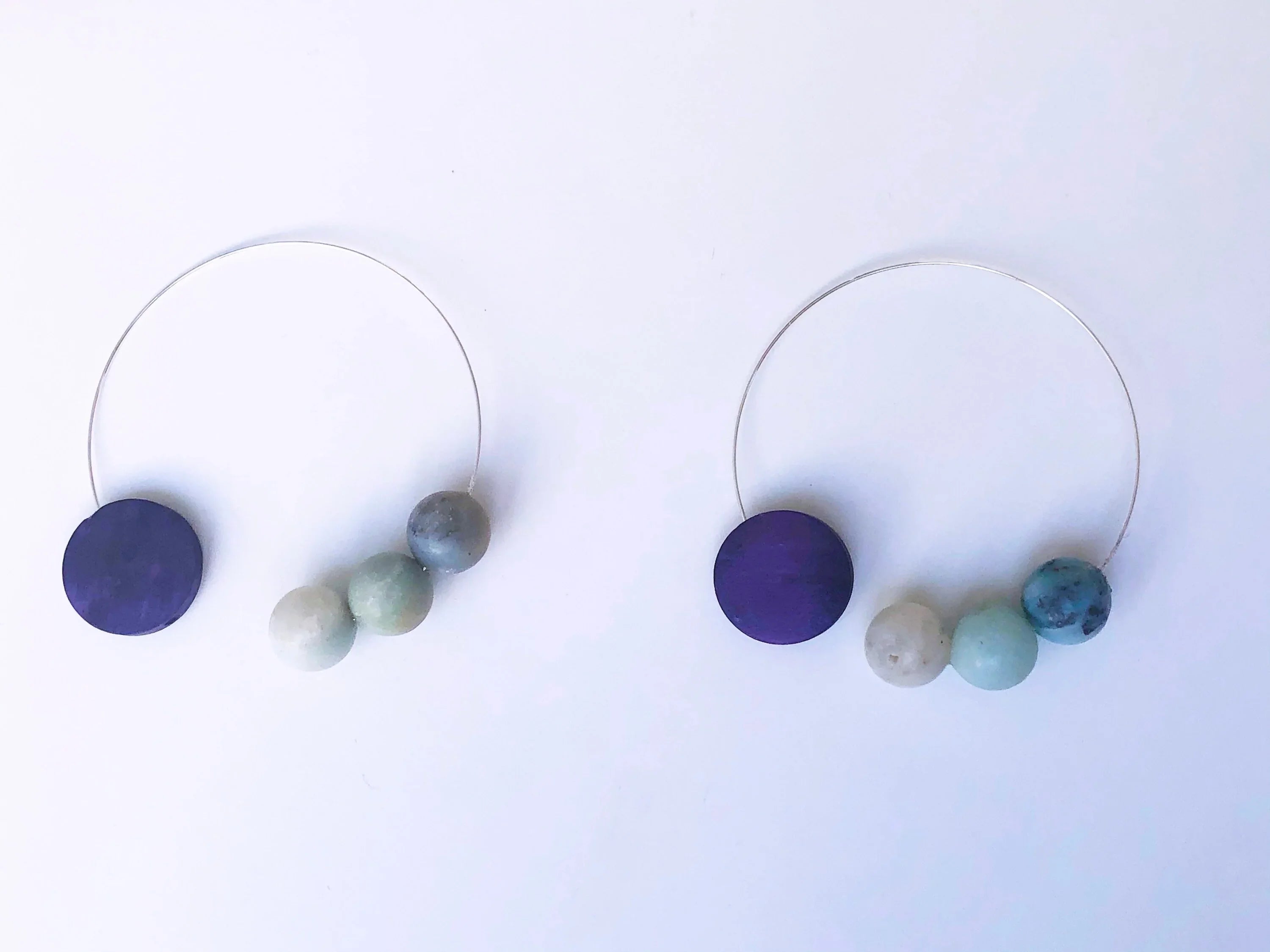 Handcrafted hoop earrings with purple disc and multicolor stone beads on white background
