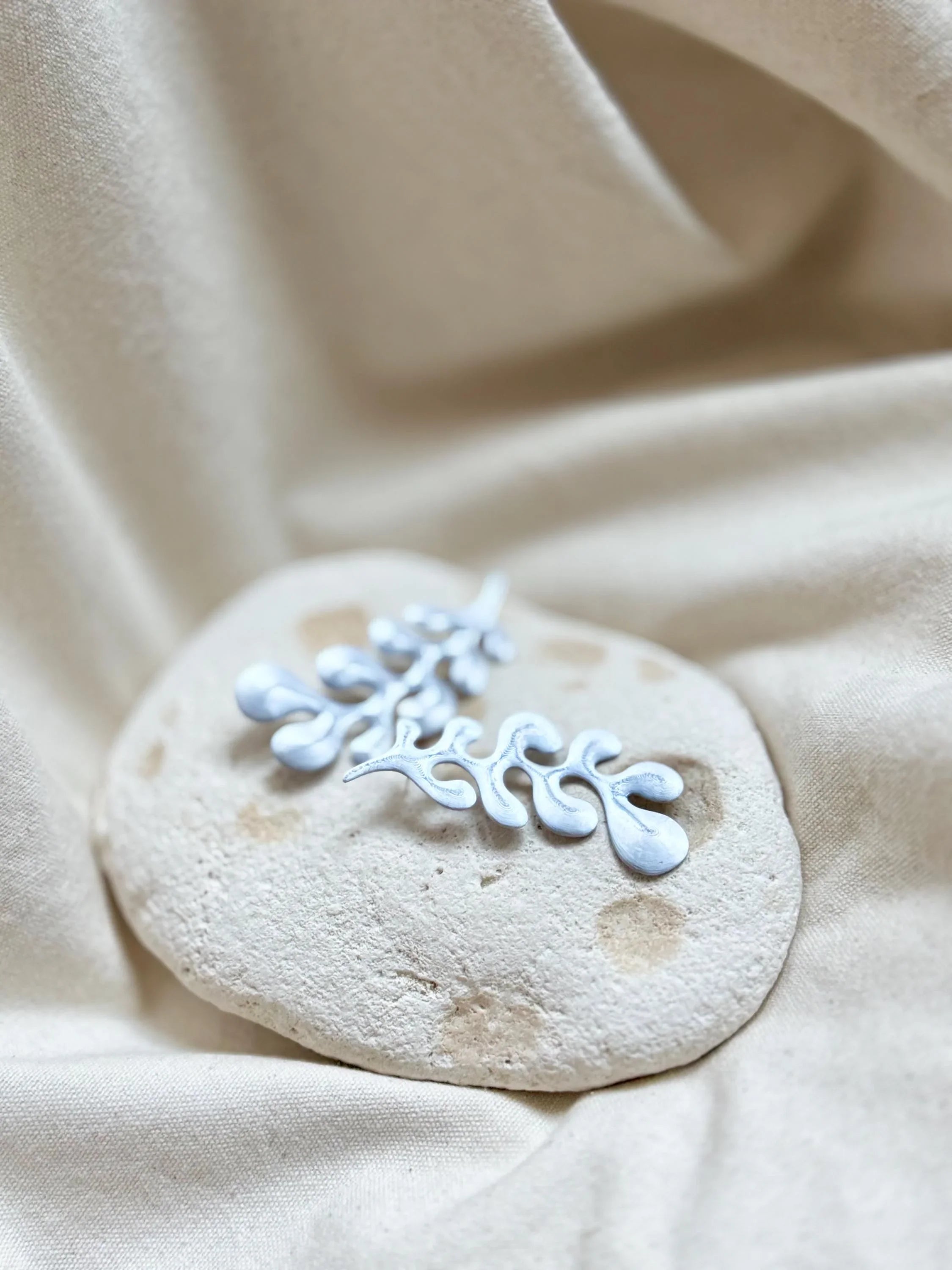 Handmade silver botanical brooch on natural stone and beige fabric background