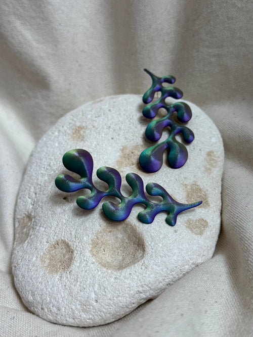 Artisan green and purple abstract earrings on a textured stone, minimalist display