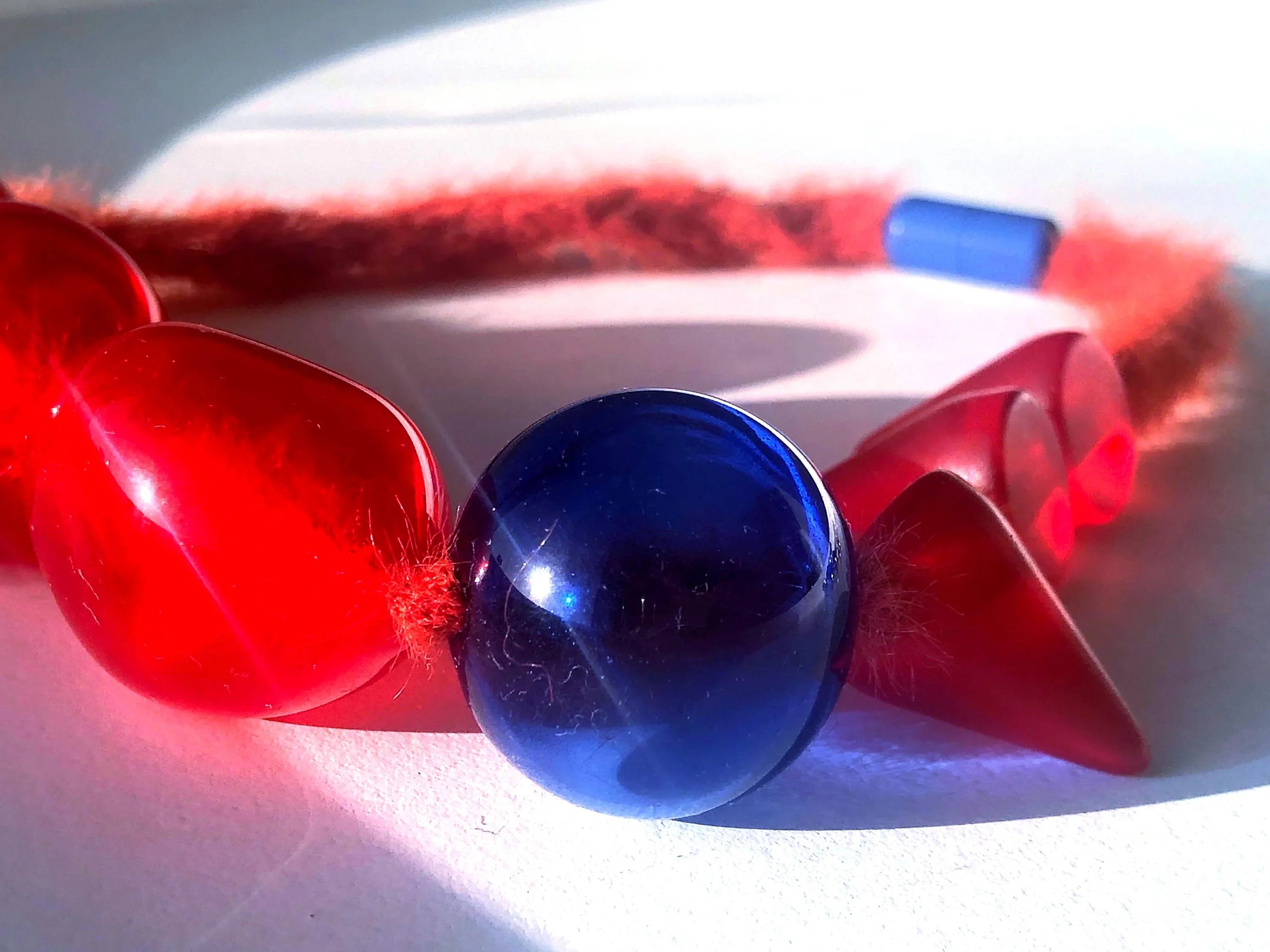 Handcrafted necklace with large red and blue geometric resin beads on a fuzzy cord