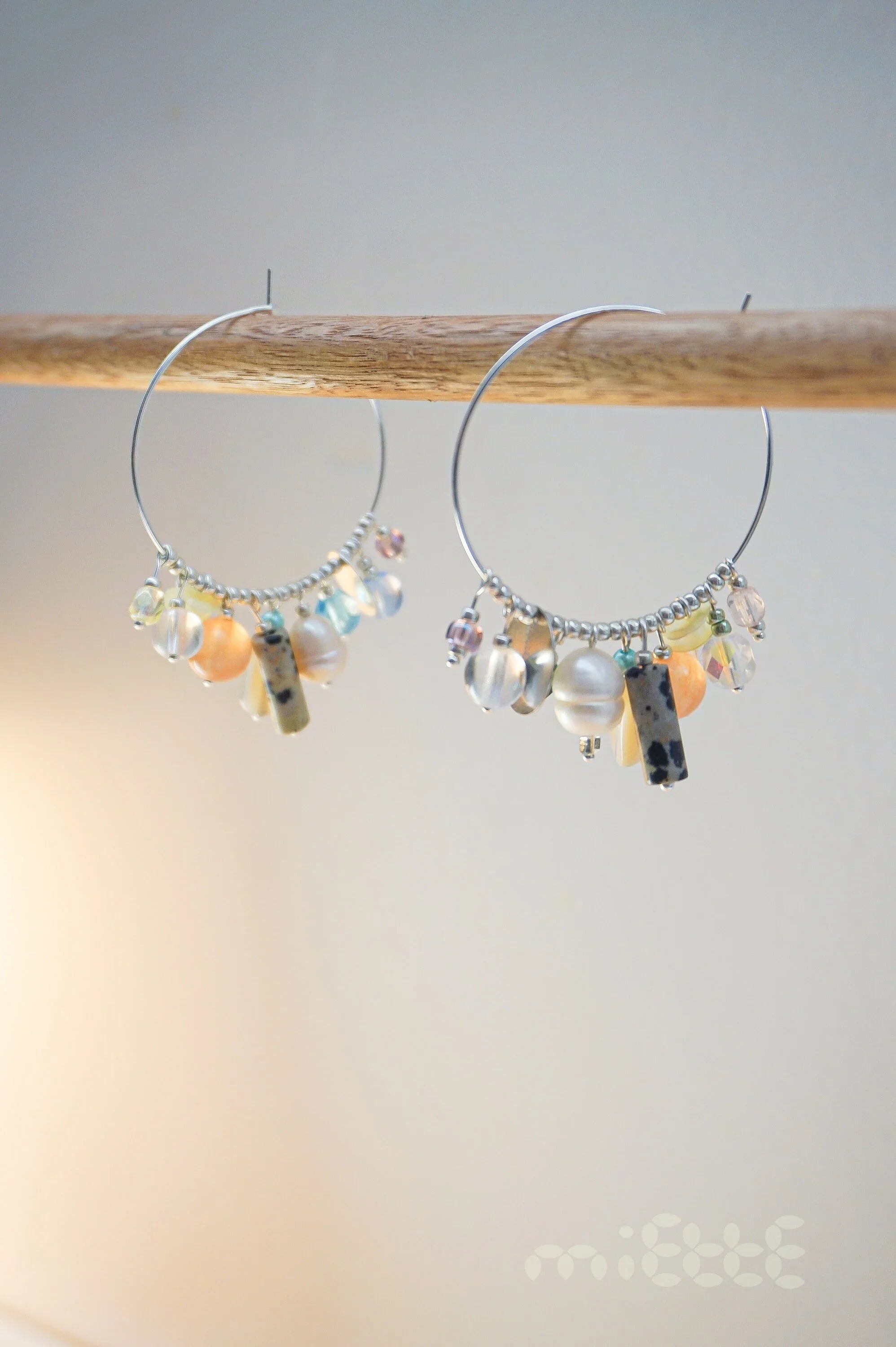 Handmade hoop earrings with multicolored beads and stones on a wooden rod