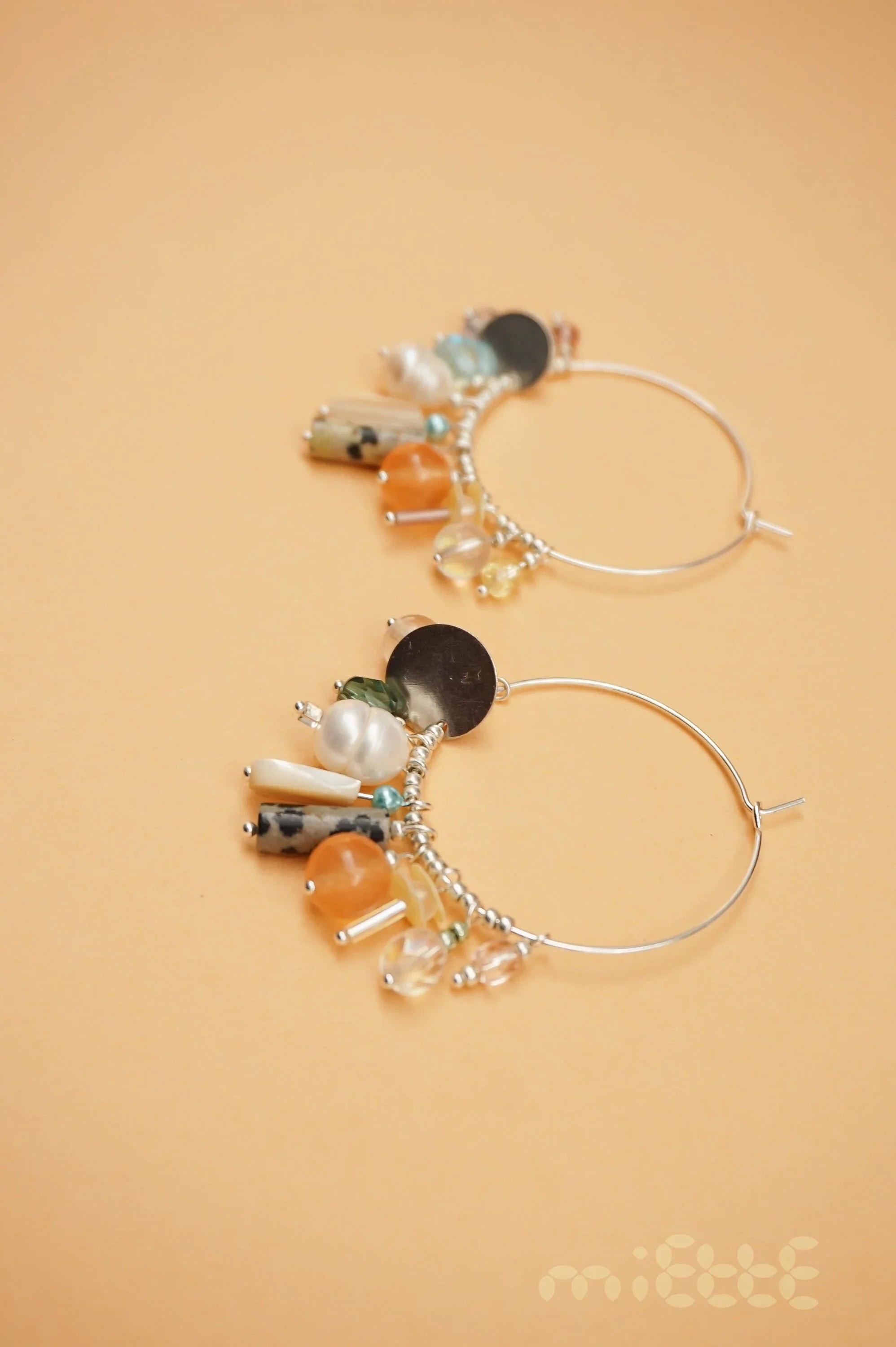 Handcrafted hoop earrings with colorful gemstone and pearl charms on a peach background