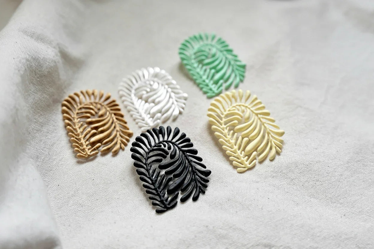Assorted artisanal leaf-shaped earrings in gold, white, mint green, black, and cream on fabric